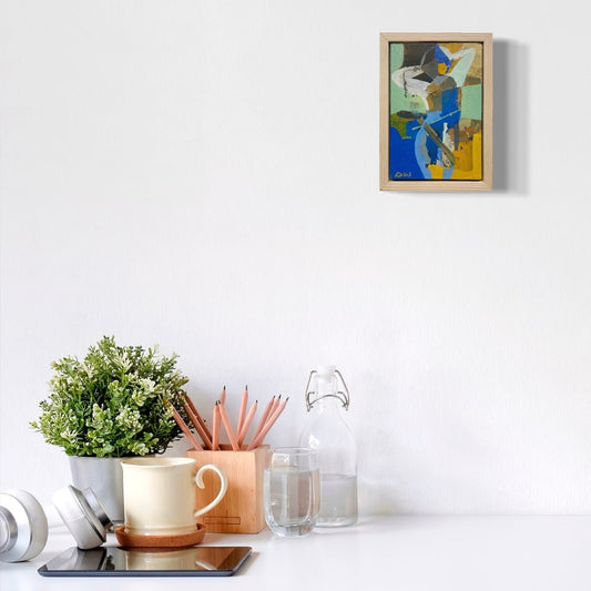 Desk setup with a plant, cups, and a framed abstract painting on a white wall.