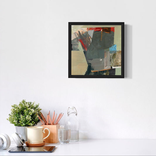 Framed abstract art piece on a white wall above a desk with office supplies.