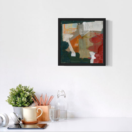 Framed abstract art piece on a white wall above a desk with office supplies.
