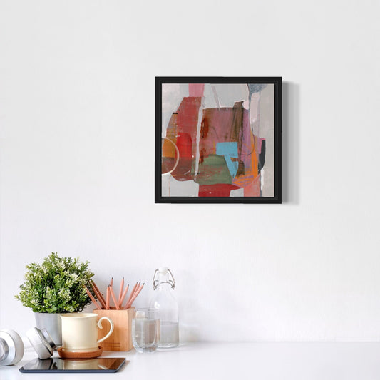 Framed abstract art piece on a white wall above a desk with office supplies.