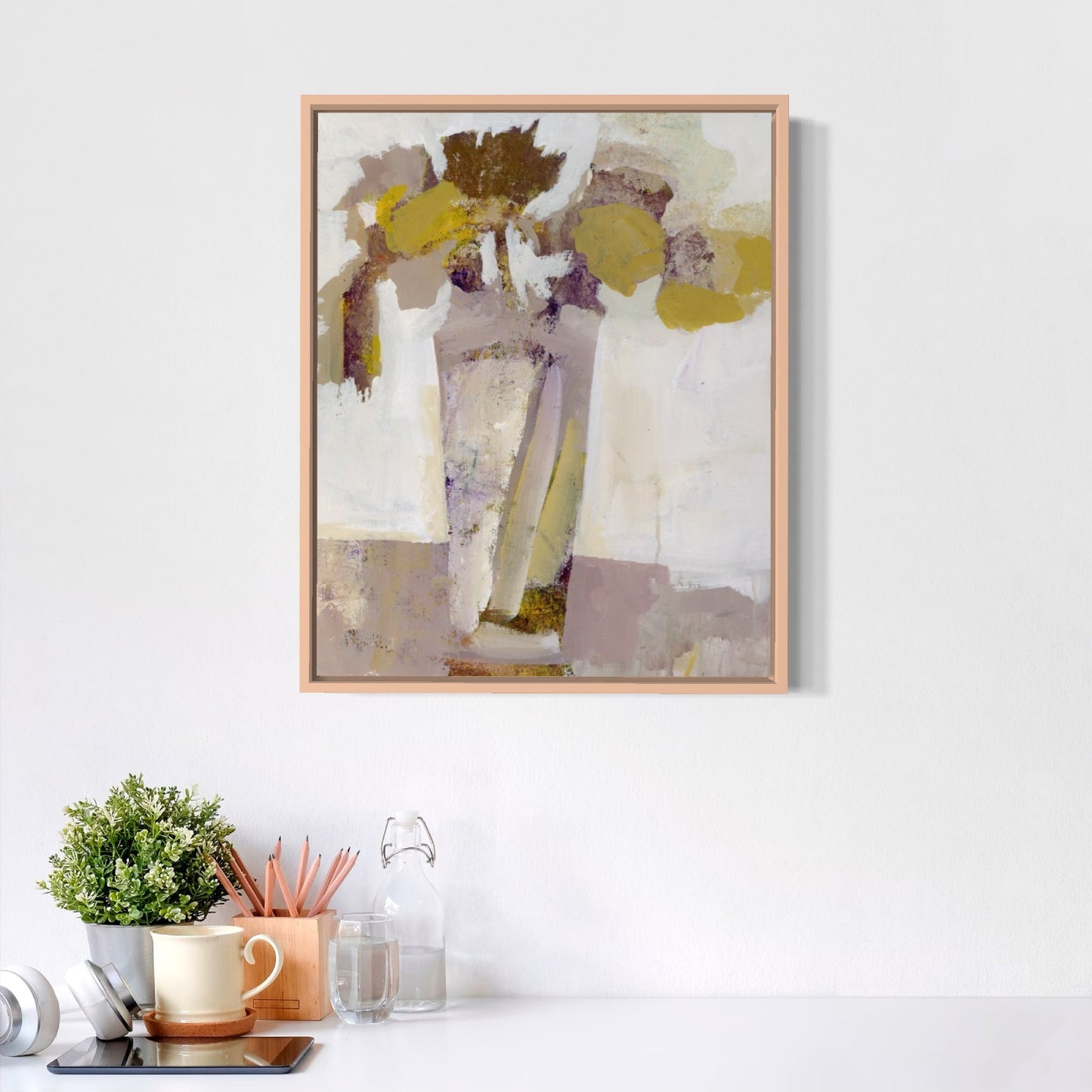Abstract art print in a wooden frame on a white wall above a desk with office supplies.