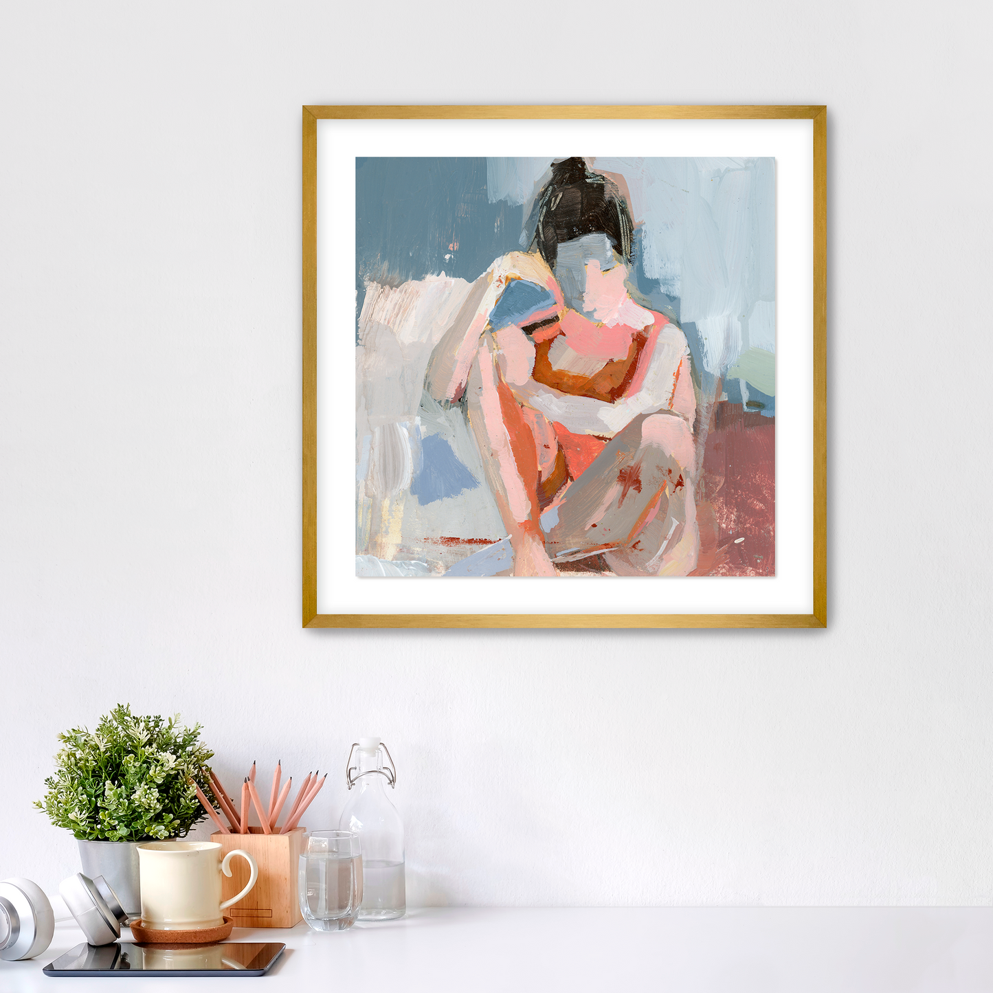 Framed abstract art print on a wall with a desk and decor items below.