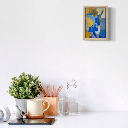 Desk setup with a plant, mug, pencils, and a framed abstract painting on a white wall.